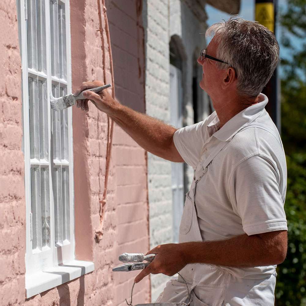 Image of a professional painter painting the exterior trim of a house as an example of how Residential Painting can improve property value